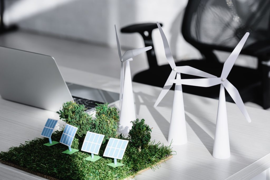 chair near table with laptop, trees, windmills, solar panels models on grass in office